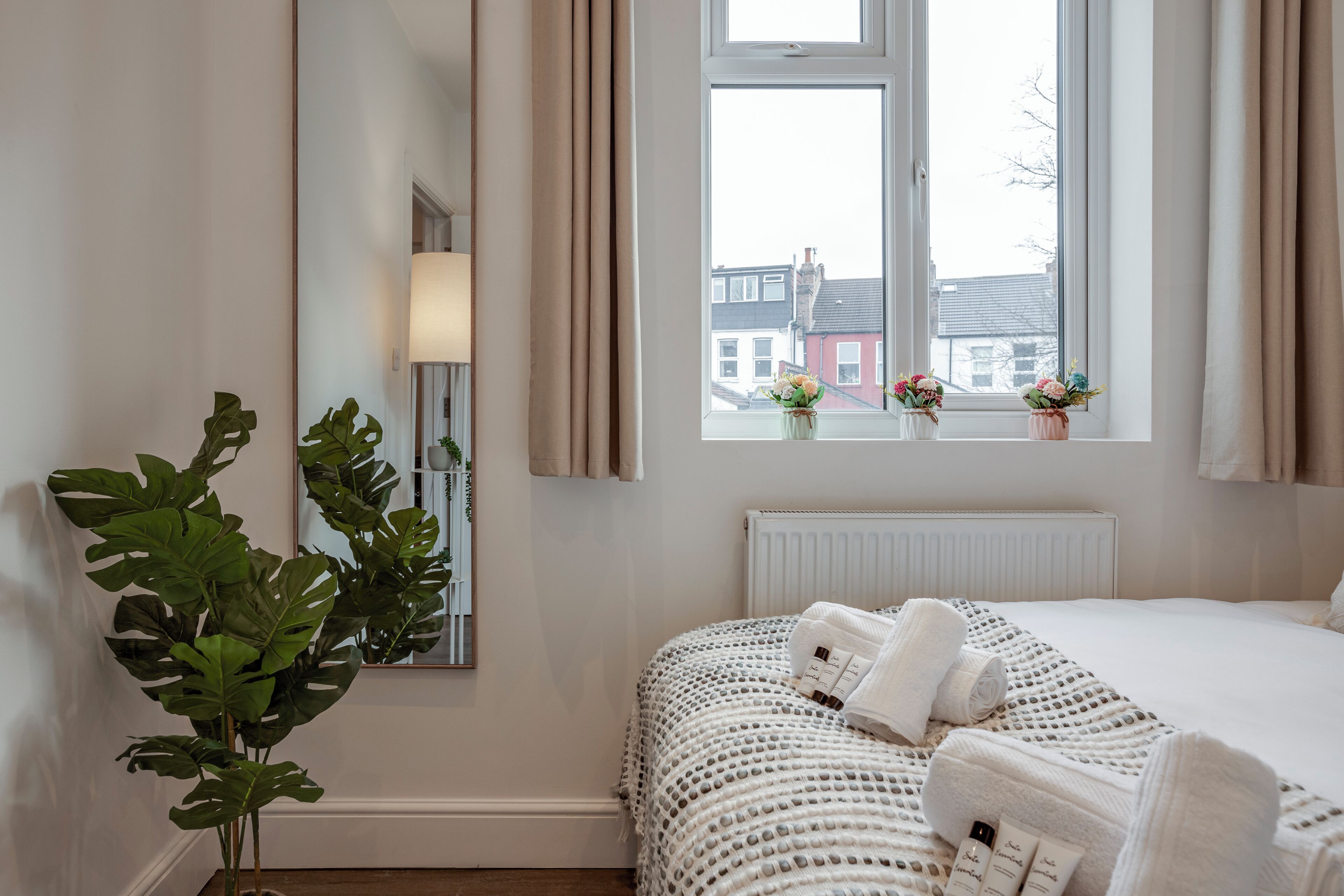Ein Schlafzimmer mit großem Fenster, einer Zimmerpflanze, einem Bett mit weißer Bettwäsche und einer Heizung.