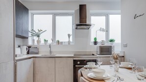 Une cuisine moderne avec un coin repas, des meubles blancs, un four encastré et une fenêtre donnant sur la ville.