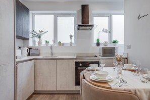 A modern kitchen with a dining area, white cabinetry, a built-in oven, and a window overlooking the city. - 2BR Modern Flat - 15 Min to Central London - Free Parking (London)