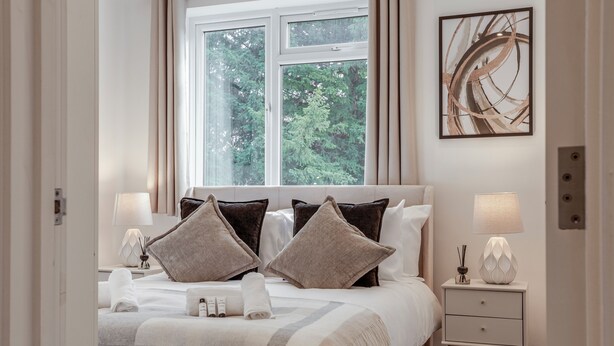 Une chambre d’hôtel avec un lit, deux tables de chevet, une fenêtre donnant sur des arbres et une œuvre d’art abstraite accrochée au mur.