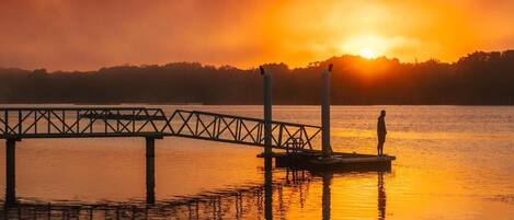 Un muelle se adentra en aguas tranquilas, con un atardecer en el fondo.