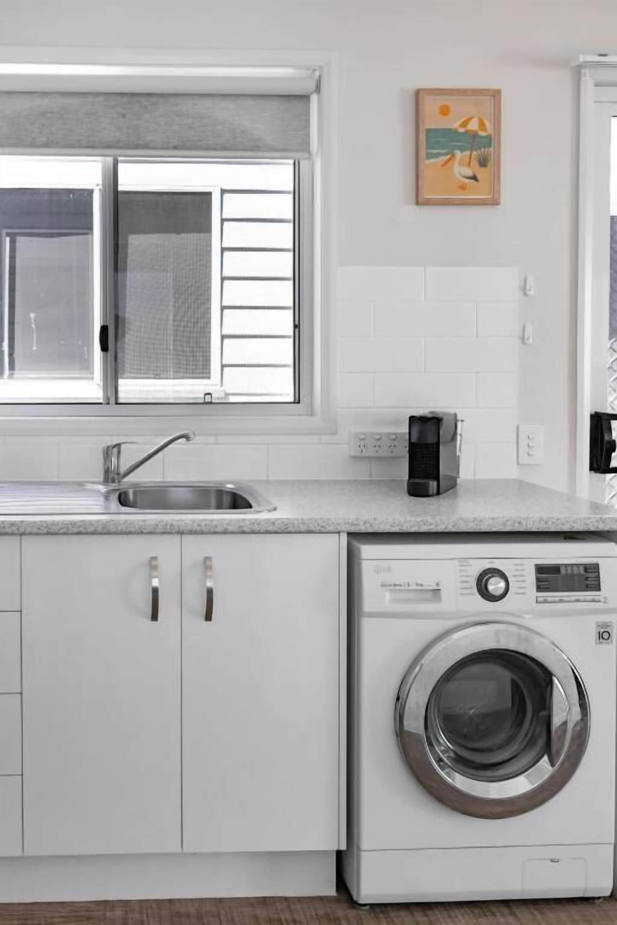 A compact kitchen with a built-in washing machine, a sink, and a window with blinds.