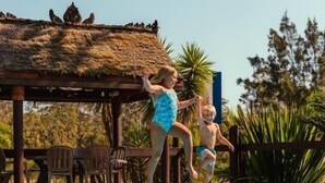 Una piscina con una struttura a tetto di paglia e sedie sullo sfondo.