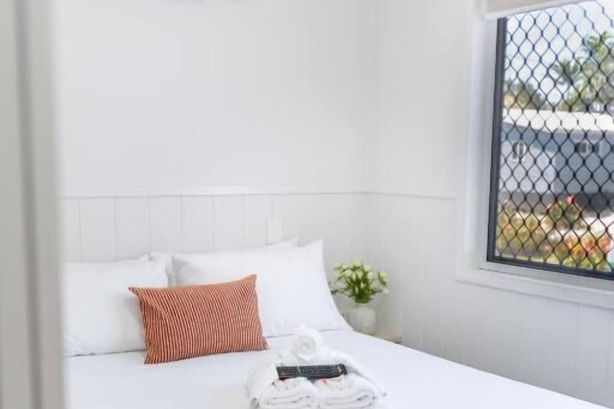 A hotel room with a bed, white walls, a window with a view, and an air conditioning unit.