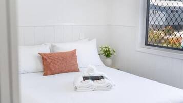 Ett hotellrum med en säng, vita väggar, ett fönster med utsikt och en luftkonditioneringsanläggning.