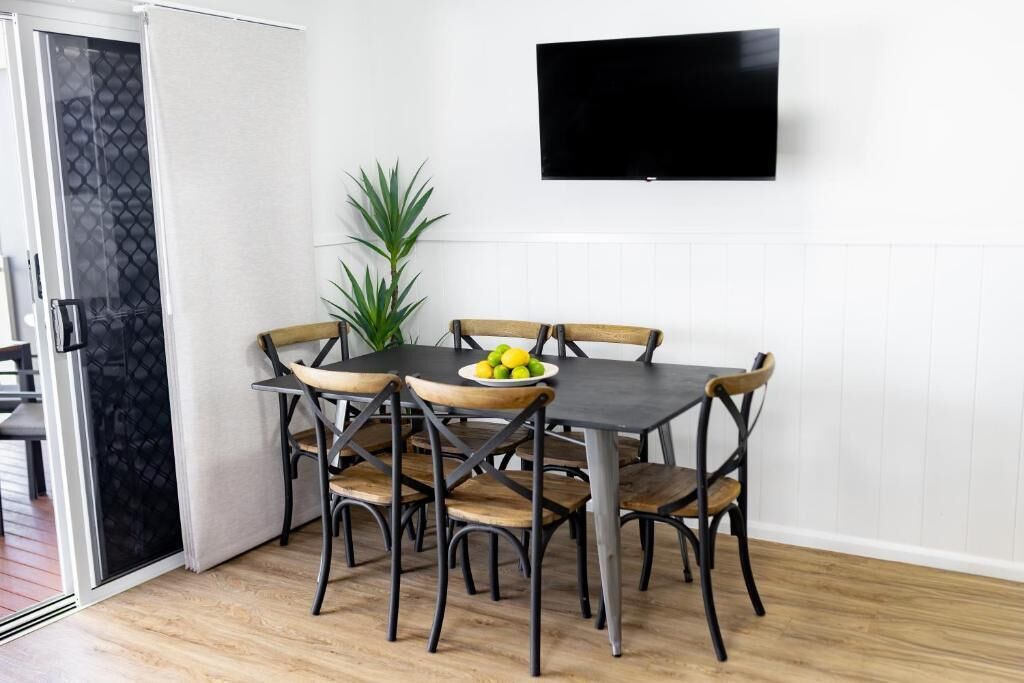 A dining area with a table and chairs, a potted plant, and a flat-screen TV mounted on the wall.