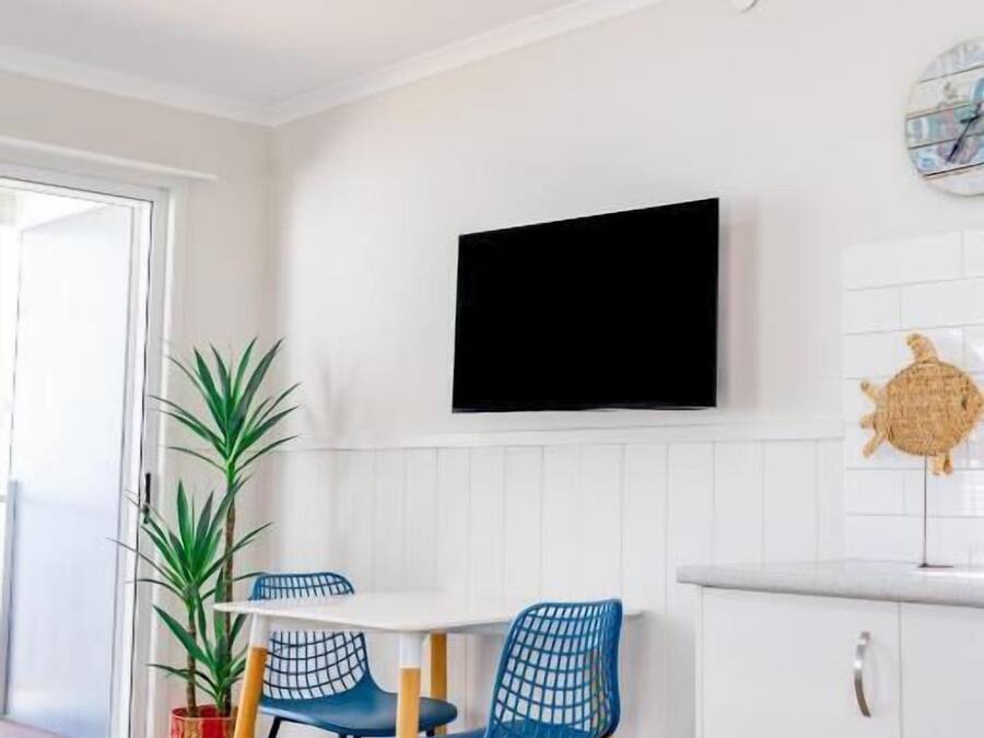 A modern kitchen with a flat-screen TV, white cabinetry, and a dining area with blue chairs.