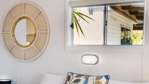 Un letto rifatto con cura, un cuscino, uno specchio tondo e una finestra con vista sul verde.