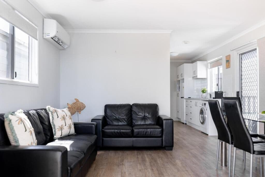 Ein modernes Wohnzimmer mit einer schwarzen Ledersofa, einem Essbereich mit Tisch und Stühlen, einer Küche mit weißen Schränken sowie einer Waschgegend.