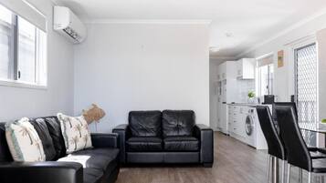 Ein modernes Wohnzimmer mit einer schwarzen Ledersofa, einem Essbereich mit Tisch und Stühlen, einer Küche mit weißen Schränken sowie einer Waschgegend.