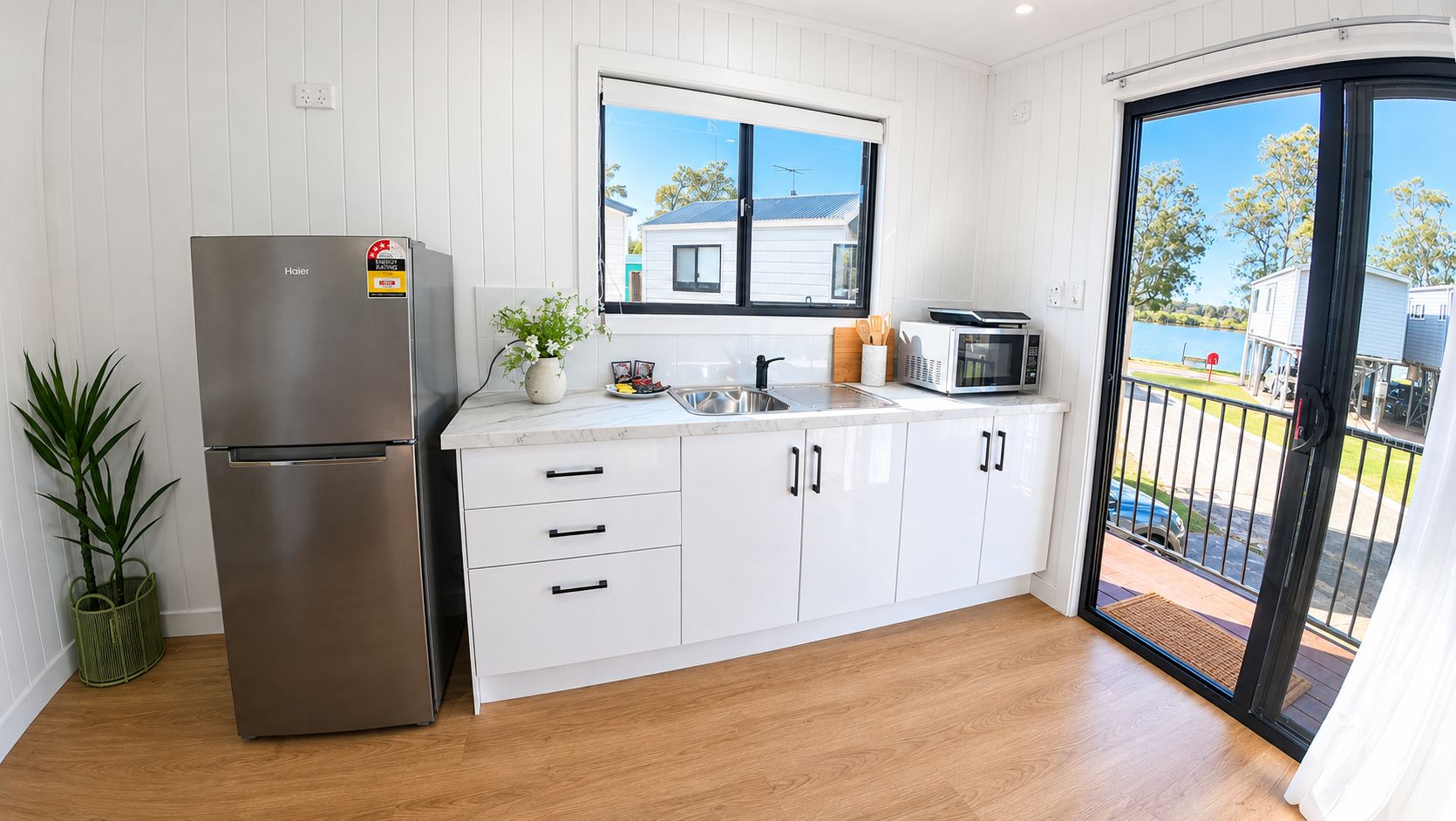 Una cocina moderna con un refrigerador de acero inoxidable, armarios blancos, un microondas y un ventanal con vista a un barrio residencial.