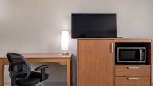 A room with a wooden desk, a black office chair, a flat-screen TV, a lamp, and a microwave. - Colorado Springs City Core Urban Stay with 2 Queen Beds (Colorado Springs)
