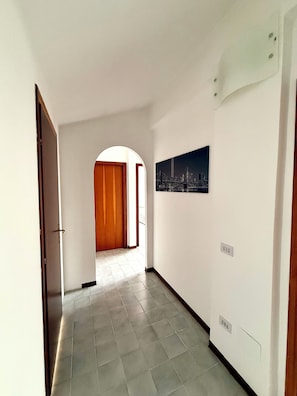 Un couloir avec un sol carrelé, une porte en bois et un tableau encadré accroché au mur.