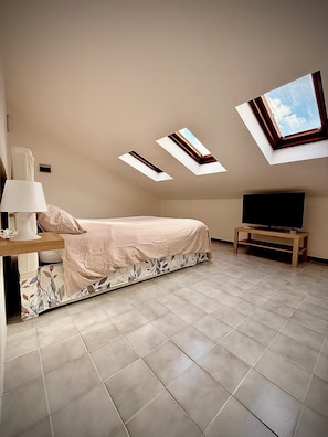 A bedroom with a bed, a TV on a stand, a lamp, and skylights.
