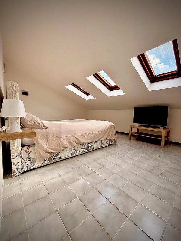 Une chambre à coucher avec un lit, un téléviseur posé sur un meuble, une lampe et des fenêtres de toit.