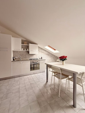 Une cuisine moderne avec des meubles blancs, une table à manger avec des chaises et une lucarne.