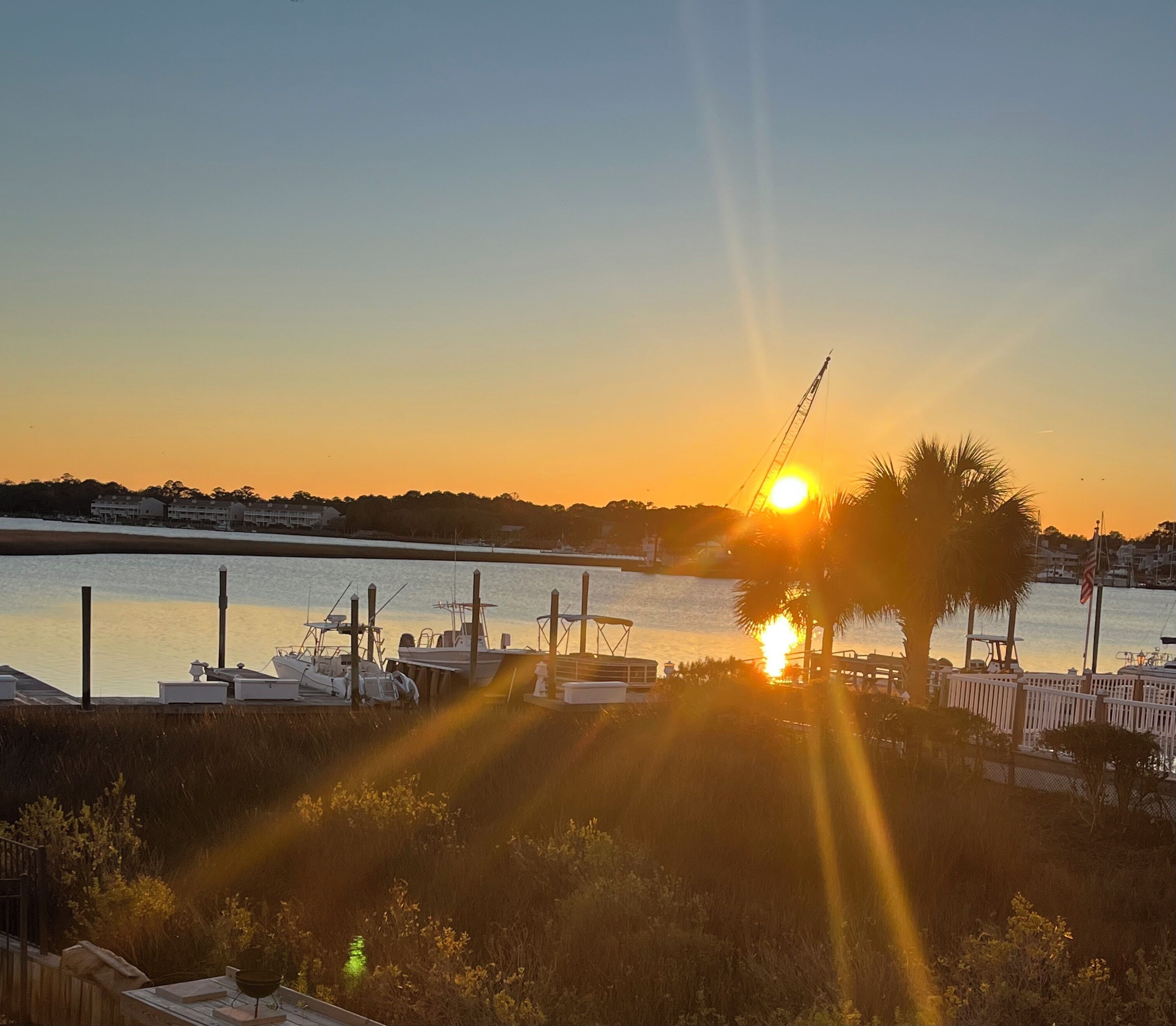 Marina com barcos atracados, pôr do sol ao fundo e uma guindaste.
