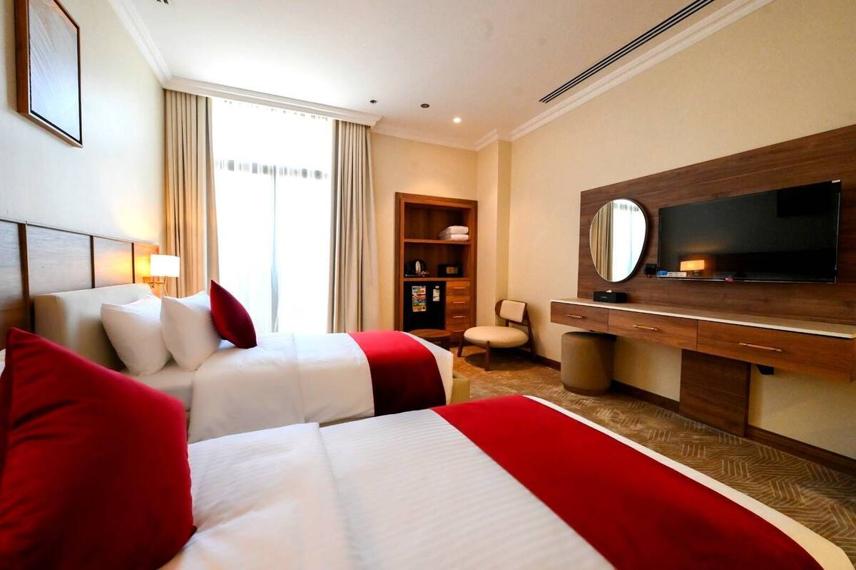 Habitación de hotel con dos camas, televisión, escritorio, silla, armario y ventana con cortinas.