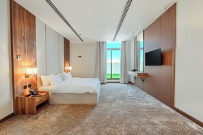 A hotel room with a bed, bedside lamps, a TV, a desk, and a view of the outdoors. - Teela Hotel (Madinah)