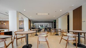En modern inredning med runda bord och stolar, en reception och ett kök i bakgrunden.