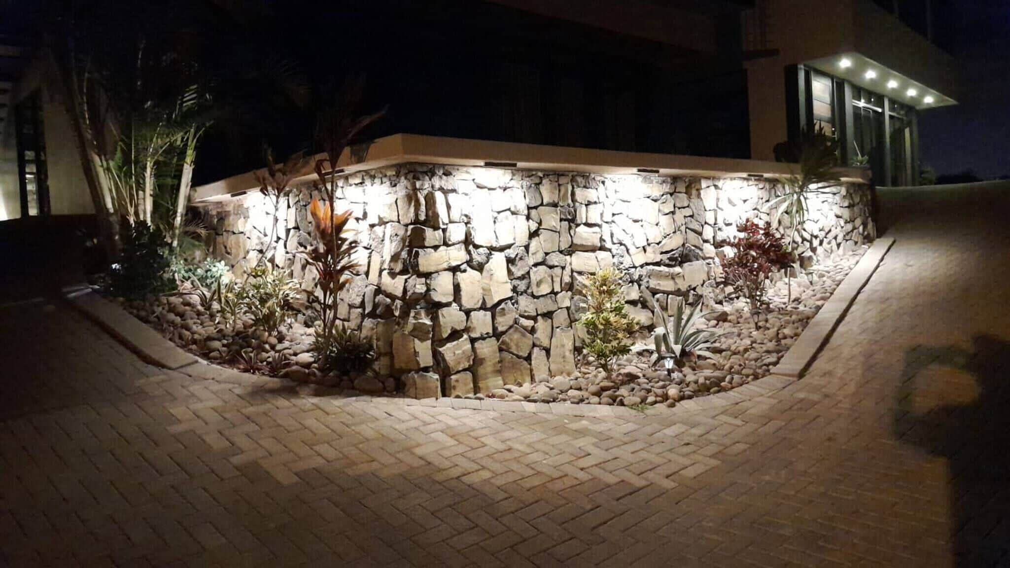 A stone wall with plants and a paved area.