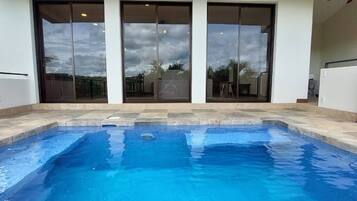 A swimming pool with a tiled deck, large sliding glass doors, and a view of the surrounding area.