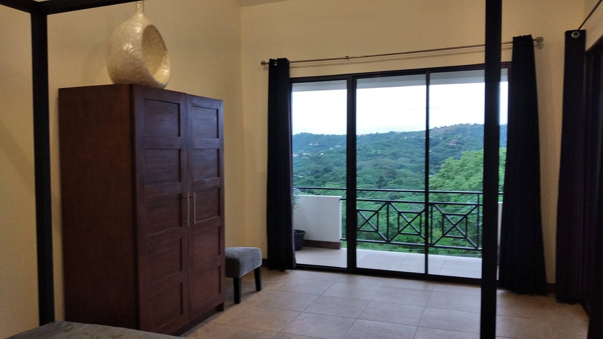A room with a large sliding glass door leading to a balcony with a view of a green landscape.