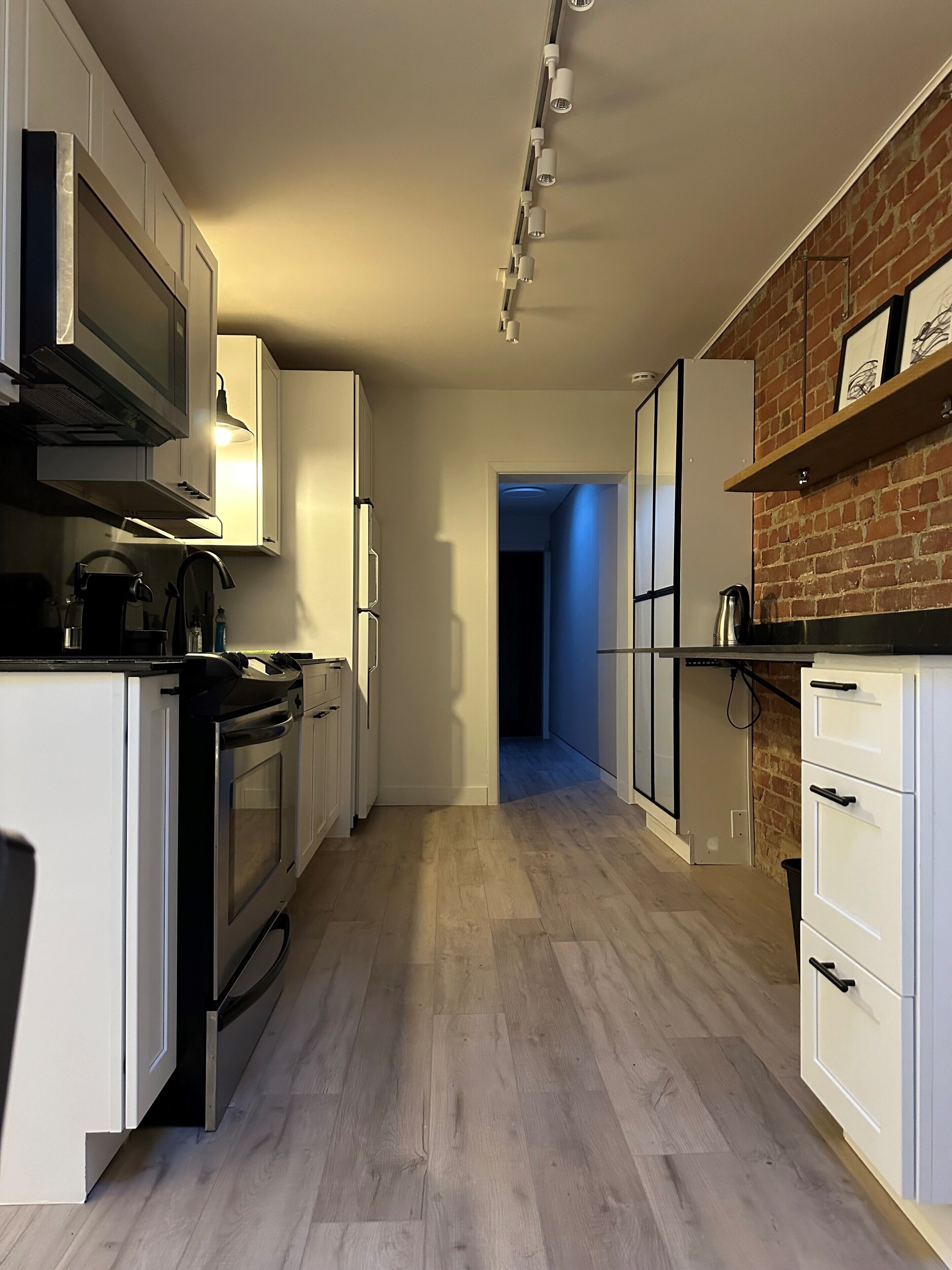 A modern kitchen with white cabinetry, a built-in oven, and a brick accent wall.