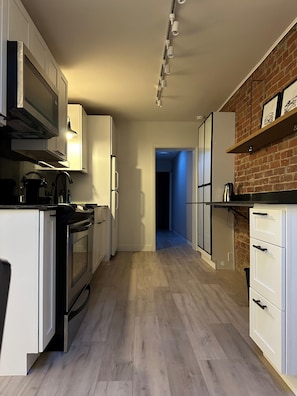 A modern kitchen with white cabinetry, a built-in oven, and a brick accent wall. - Toronto Cork Town, Queen St.E, Spacious 2nd Fl. Loft (Toronto)