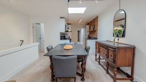 Een moderne eetruimte met een lange tafel, stoelen, een houten buffetkast en een spiegel aan de muur.