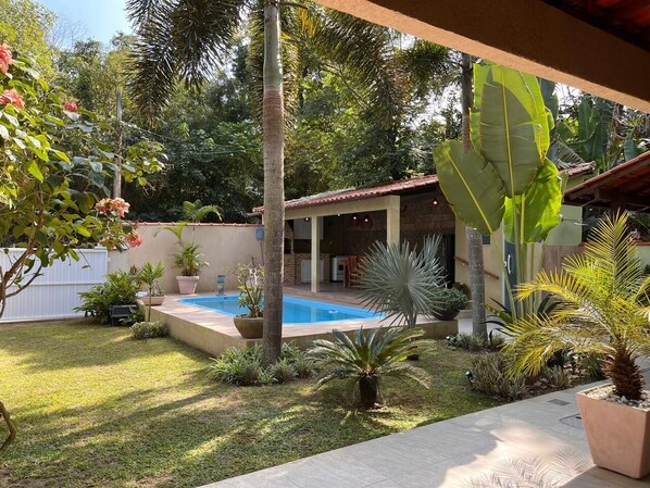 A pool area with a covered patio, surrounded by various potted plants and a small garden.