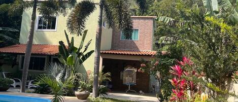 A house with a swimming pool, surrounded by lush greenery and a small dog.