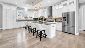 A modern kitchen with white cabinetry, a central island with bar stools, stainless steel appliances, and pendant lighting. - 🦩Book Me Baby! Sea Breeze Escape in Santa Rosa Beach🦩 (Santa Rosa Beach)