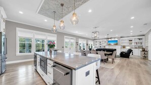 A spacious kitchen with a large island, white cabinetry, and a dining area with a black sofa. - 🦩Book Me Baby! Sea Breeze Escape in Santa Rosa Beach🦩 (Santa Rosa Beach)