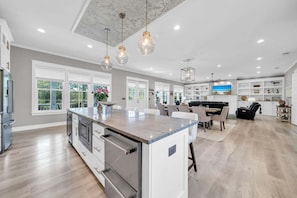 A spacious kitchen with a large island, white cabinetry, and a dining area with a black sofa. - 🦩Book Me Baby! Sea Breeze Escape in Santa Rosa Beach🦩 (Santa Rosa Beach)