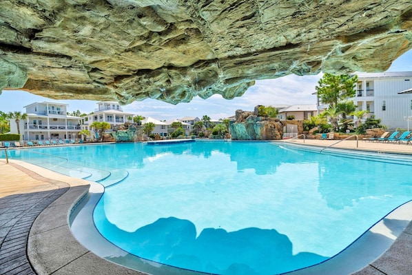A swimming pool with a rocky overhang, poolside lounge chairs, and a view of residential buildings. - 🦩Book Me Baby! Sea Breeze Escape in Santa Rosa Beach🦩 (Santa Rosa Beach)