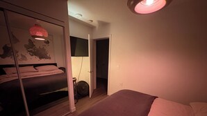 Ein Schlafzimmer mit einem Bett, einem Kleiderschrank, einem Ventilator und einer Tür zu einem anderen Raum.