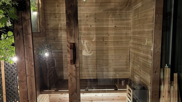 Eine Sauna mit Holzwänden und einer Glastür, eine kleine Sitzbank und eine Wasserflasche.
