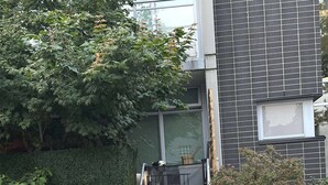 Ein Wohngebäude mit einer Betonstiege, die zu einer Tür, einem Metallgitter und einem Hecken führt.