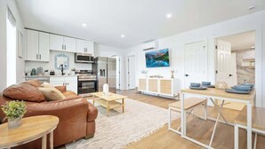 A modern living room with a brown leather sofa, a wooden coffee table, and a kitchen area with white cabinets and a microwave.