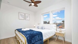 A bedroom with a bed, a ceiling fan, a window with a view, and a bedside table.
