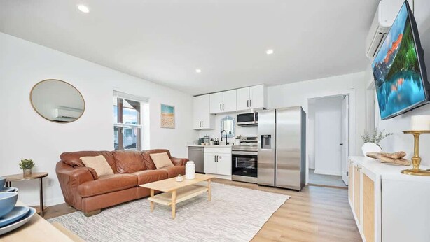 A modern kitchen with stainless steel appliances, a brown leather sofa, and a flat-screen TV.