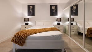 A modern bedroom with a bed, nightstands, a mirror, and wall art. - Waterline Poolside Apartment (Agnes Water)