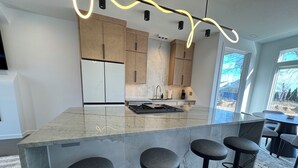 Una cocina moderna con una isla de mármol, taburetes de bar y vistas al exterior.