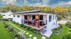 Una casa moderna de dos pisos con un porche cubierto, un césped cuidado y un jardín.
