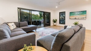 A modern living room with grey sofas, a coffee table, and a large window with a view of greenery. - Coastal Haven - Agnes Water (Agnes Water)