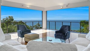 Ett modernt rum med ett glasbord, två stolar och en soffa. Det har ett stort fönster med utsikt över havet.