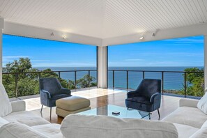 Ein modernes Zimmer mit einem Glastisch, zwei Stühlen und einer Couch. Es bietet ein großes Fenster mit Blick auf das Meer.