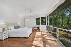 Ein modernes Schlafzimmer mit einem großen Bett, einem Schreibtisch und Blick auf den Wald.