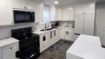 Une cuisine moderne avec des meubles blancs, une cuisinière noire, un four à micro-ondes et un réfrigérateur.